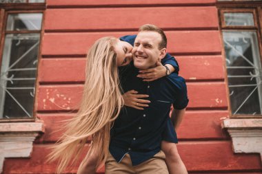 Genç bir çiftin mutlu hali kırmızı bir duvarın arkasında, kız adamın üzerine atladı.