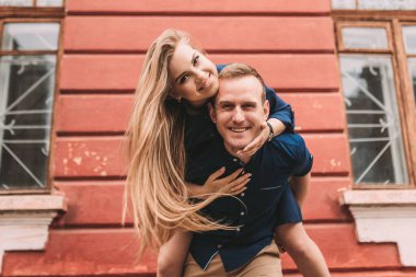 Genç bir çiftin mutlu hali kırmızı bir duvarın arkasında, kız adamın üzerine atladı.