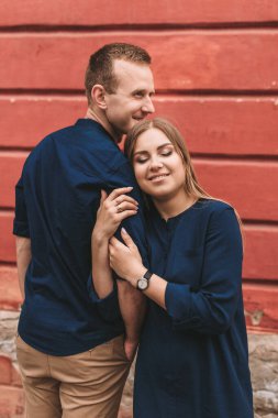 Kırmızı bir duvarın arkasında mutlu bir aile. Genç kadın başını erkeğinin omzuna koydu.