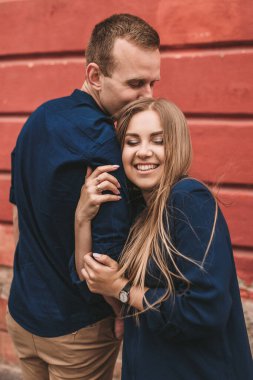 Kırmızı bir duvarın arkasında mutlu bir aile. Genç kadın başını erkeğinin omzuna koydu.