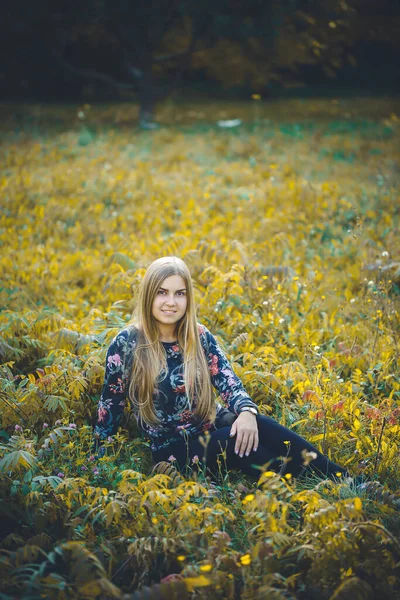 秋の自然の中で落ち葉と座ってセーターやズボンの美しい女性 明るい若い長髪の女の子は秋に赤い黄色の葉で公園でリラックスします ロマン主義 — ストック写真