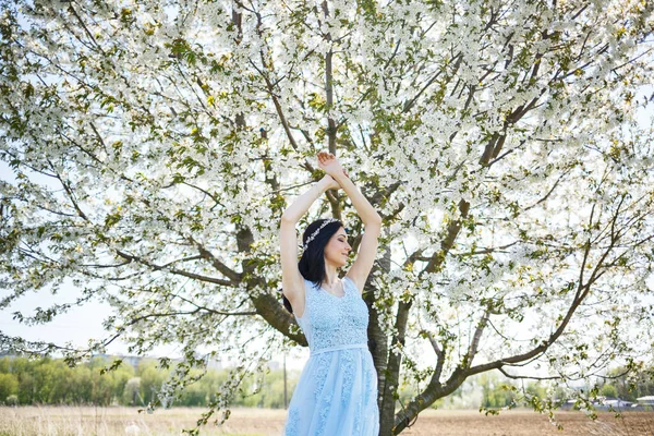 公園の緑の葉を背景にポーズをとった花束と青い光のドレスでヴィンテージのフープを持つ美しいメイクアップを持つ若い女性 新鮮な肖像画魅力的な女の子とともに白い花 — ストック写真
