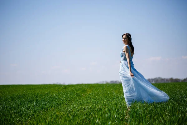 緑のフィールドの背景に青い長いドレスの女性 彼女の顔に笑顔で美しい女の子のファッションの肖像画 — ストック写真