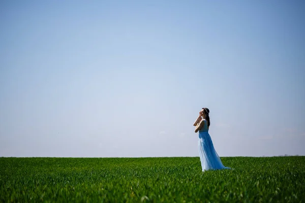 緑のフィールドの背景に青い長いドレスの女性 彼女の顔に笑顔で美しい女の子のファッションの肖像画 — ストック写真