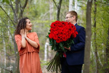 Ormanda düğün geçmişi: bir adam sürpriz yaptı, bir yüzük güzel bir kıza aşkını ilan etti ve evlenme teklifi etti. Yüzünde bir gülümseme ve bir buket kırmızı gül olan bir kız.