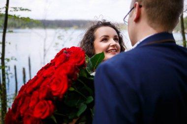 Gençlerin romantik buluşması. Takım elbiseli bir adam elinde bir buket kırmızı gülle kıza bir buket verir ve ormanda öpüşürler.