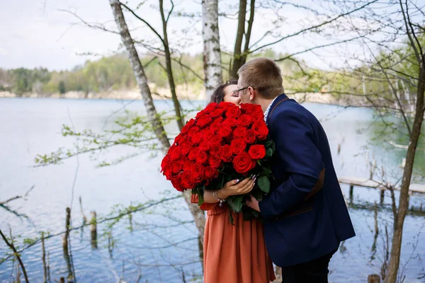 若者のロマンチックな出会い 赤いバラの花束でスーツの男は女の子に花束を与え 彼らは森の中でキスをします — ストック写真