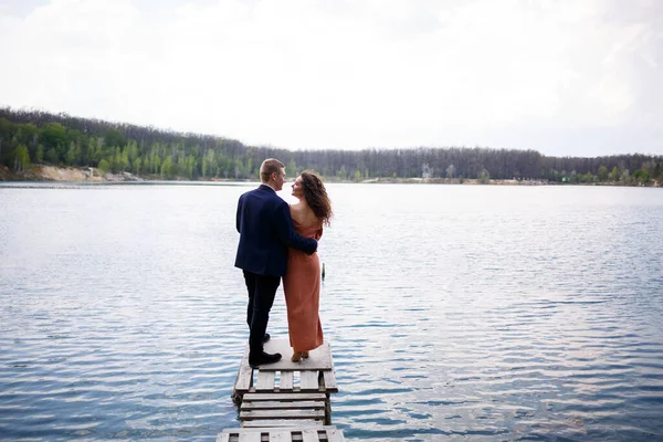 青い湖の真ん中にある木製の橋の上で手をつないでいる若いカップル 木々の背景に島の石工 ロマンスと愛幸せなカップル — ストック写真