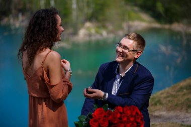 Ormanda düğün geçmişi: bir adam sürpriz yaptı, bir yüzük güzel bir kıza aşkını ilan etti ve evlenme teklifi etti. Yüzünde bir gülümseme ve bir buket kırmızı gül olan bir kız.