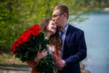 Gençlerin romantik buluşması. Genç bir kadın erkeğiyle evlenmeyi kabul etti. Takım elbiseli bir adam elinde bir buket kırmızı gülle kıza bir buket verir ve ormanda öpüşürler.