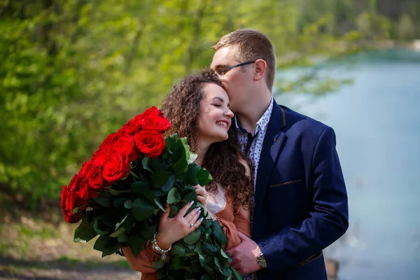 年轻人的浪漫聚会 一个年轻的女人同意嫁给她的男人 一个穿着西服 捧着一束红玫瑰的男人送给女孩一束红玫瑰 女孩们在森林里接吻 — 图库照片