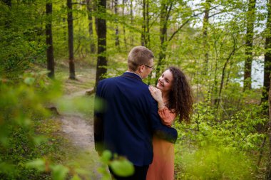 Yeşil bir ormanda genç bir çiftin romantik yürüyüşü, ılık bahar havası. Erkek ve kız doğada sarılıyorlar.