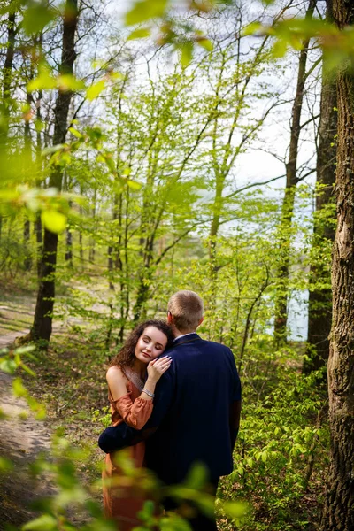 Romantic walk of a young couple in a green forest, warm spring weather. Guy and girl hugging in nature