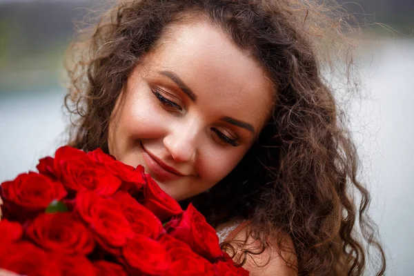 곱슬곱슬 머리에 얼굴에 미소를 머금은 매력적 소녀가 배경에 커다란 꽃다발을 — 스톡 사진