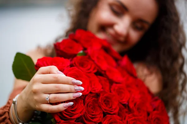 红玫瑰花束上的一个戴着结婚戒指的女孩的手 — 图库照片