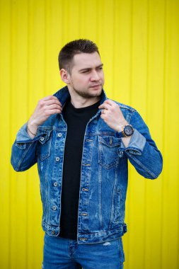 Yakışıklı, şık bir adamın portresi. Siyah, boş tişört giymiş bir adam. Arka planda sarı bir duvarda duruyor. Şehir tarzı kıyafetler, modern moda imajı. Erkek modası