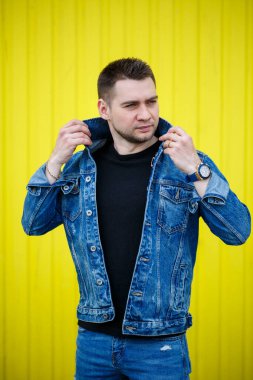 Yakışıklı, şık bir adamın portresi. Siyah, boş tişört giymiş bir adam. Arka planda sarı bir duvarda duruyor. Şehir tarzı kıyafetler, modern moda imajı. Erkek modası