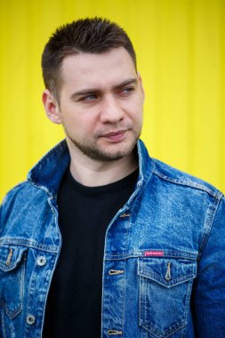 Yakışıklı, şık bir adamın portresi. Siyah, boş tişört giymiş bir adam. Arka planda sarı bir duvarda duruyor. Şehir tarzı kıyafetler, modern moda imajı. Erkek modası