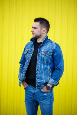 Yakışıklı, şık bir adamın portresi. Siyah, boş tişört giymiş bir adam. Arka planda sarı bir duvarda duruyor. Şehir tarzı kıyafetler, modern moda imajı. Erkek modası
