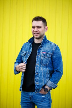 Yakışıklı, şık bir adamın portresi. Siyah, boş tişört giymiş bir adam. Arka planda sarı bir duvarda duruyor. Şehir tarzı kıyafetler, modern moda imajı. Erkek modası