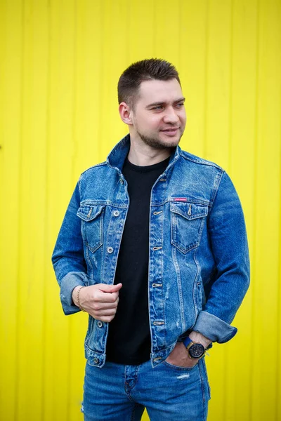 Yakışıklı, şık bir adamın portresi. Siyah, boş tişört giymiş bir adam. Arka planda sarı bir duvarda duruyor. Şehir tarzı kıyafetler, modern moda imajı. Erkek modası