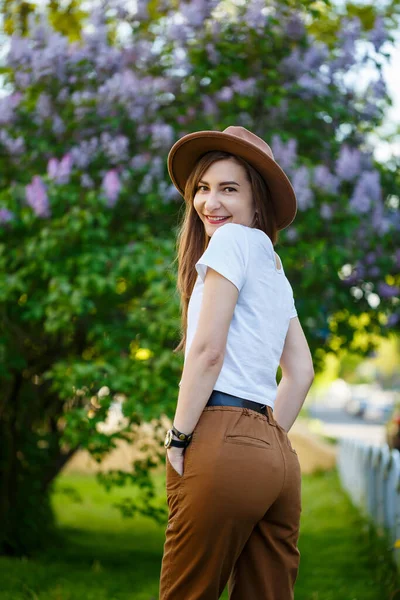 Bella Ragazza Con Cappello Marrone Piedi Vicino Cespuglio Lilla Elegante — Foto Stock