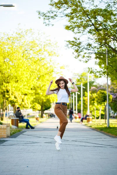 帽子を被った若い幸せな女性が公園の路地を歩いている 明るい晴れた夏の日に彼女の顔に笑顔でヨーロッパの外観の女の子 — ストック写真