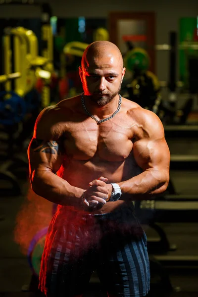 Sporty handsome strong man posing on the background of the gym. A strong bodybuilder with perfect abs, shoulders, biceps, triceps and chest.