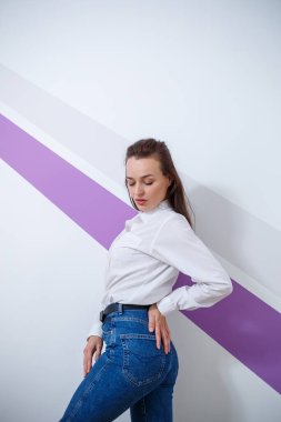 Güzel, beyaz tenli, beyaz tişörtlü, açık renk pantolonlu, mor çizgili bir kız.