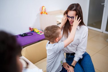 Doktor steteskoptaki hasta bir çocuğun akciğerlerini dinliyor. Annesiyle birlikte doktora geldi. Kız soğuk algınlığından hasta. Doktorun ışık odasındalar..