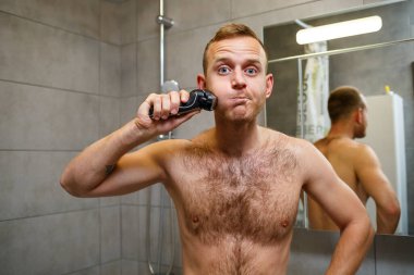 Bir adam aynanın önünde yüzünü jiletle traş eder. Deri tahrişi. Banyo prosedürü