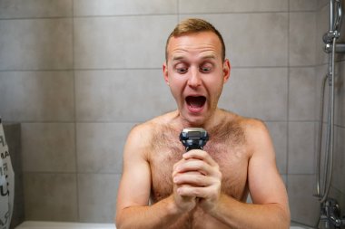 Bir adam aynanın önünde yüzünü jiletle traş eder. Deri tahrişi. Banyo prosedürü