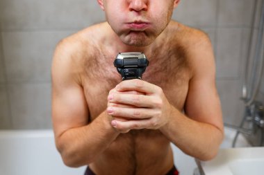Bir adam aynanın önünde yüzünü jiletle traş eder. Deri tahrişi. Banyo prosedürü