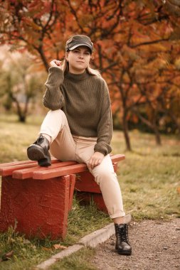 Güz parkında, şık kıyafetler, yeşil kazak ve bej pantolon giyen güzel bir kız.