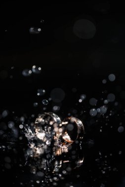 Yeni evliler için altın alyanslar. Düğün gününde, siyah bir zeminde, su damlalarıyla. Mücevherler