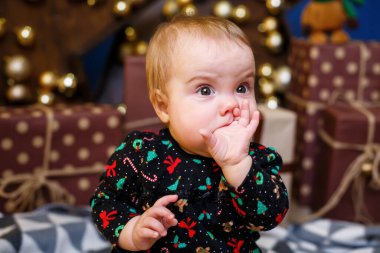 Küçük kız Noel ağacının arka planında yerde oturuyor. Mutlu çocuk. Yeni yıl odası dekorasyonları