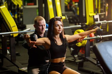 Spor salonunda antrenörle egzersiz yapan bir kız.