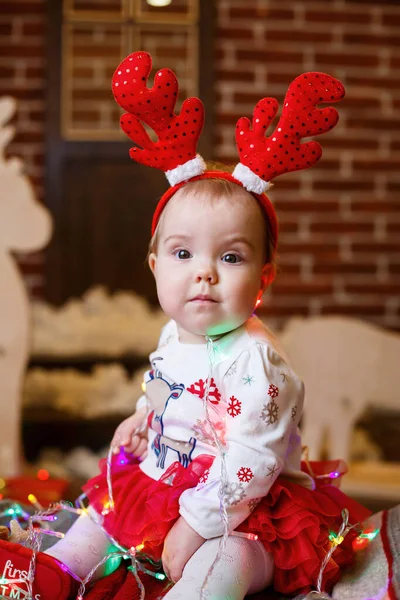 暖かいセーターを着た少女がクリスマスツリーの下に座っておもちゃや贈り物を頭に角をつけています 幸せな子供時代 年末年始の雰囲気 — ストック写真