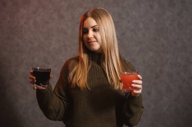 Kız yeşil bir kazak giymişti ve elinde kırmızı ve siyah bir sıvı tutuyordu..