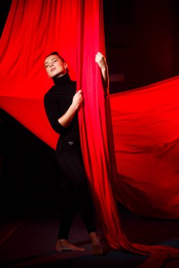 Bir kadın karanlık bir arka planda havadan akrobasi yapıyor. Spor jimnastikçisi tuvalde egzersiz yapıyor.