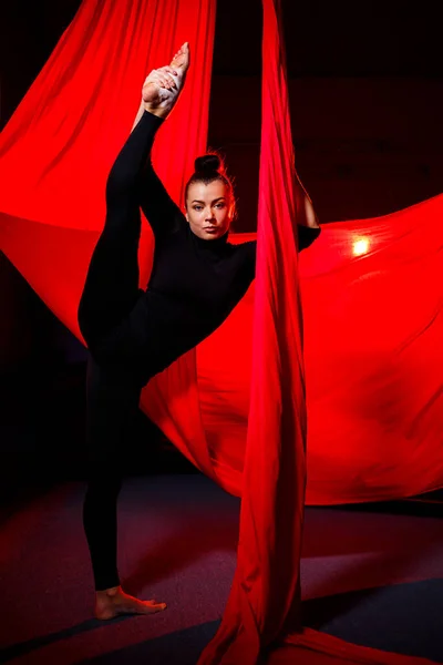 A beautiful sportive girl acrobat performs gymnastic and circus exercises on red silk. Aerial gymnastics on canvas