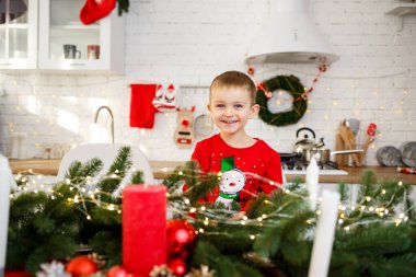 Yeni yıl için dekore edilmiş Noel masasının mutfağında oturan bir çocuğun portresi. Mutfakta Noel dekoru