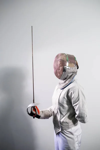 Chica con un disfraz de esgrima con una espada en la mano aislada en el fondo del estudio blanco. Las chicas jóvenes practican y hacen ejercicio. Deportes, estilo de vida saludable. —  Fotos de Stock