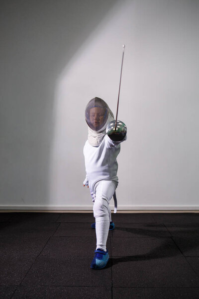 A girl in a fencing suit with a sword in hand. Young female model practicing and exercising. Sports, healthy lifestyle.