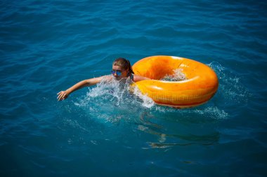 Güzel genç bir kadın şişirilebilir bir çemberden mavi denize düştü. Tatildeki kız denizde daireler çizerek yüzüyor