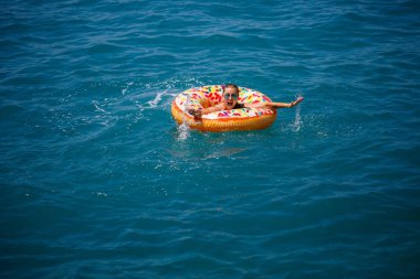 Şeffaf turkuaz denizde şişme bir çöreğin üzerinde yüzen genç bir kadın. İnce bir bayanın Türkiye, Mısır ve Akdeniz 'de tatil yaparken dinlenmesi.