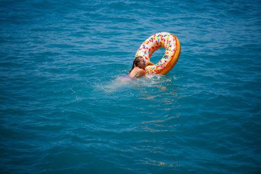 Şeffaf turkuaz denizde şişme bir çöreğin üzerinde yüzen genç bir kadın. İnce bir bayanın Türkiye, Mısır ve Akdeniz 'de tatil yaparken dinlenmesi.