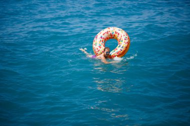 Şeffaf turkuaz denizde şişme bir çöreğin üzerinde yüzen genç bir kadın. İnce bir bayanın Türkiye, Mısır ve Akdeniz 'de tatil yaparken dinlenmesi.