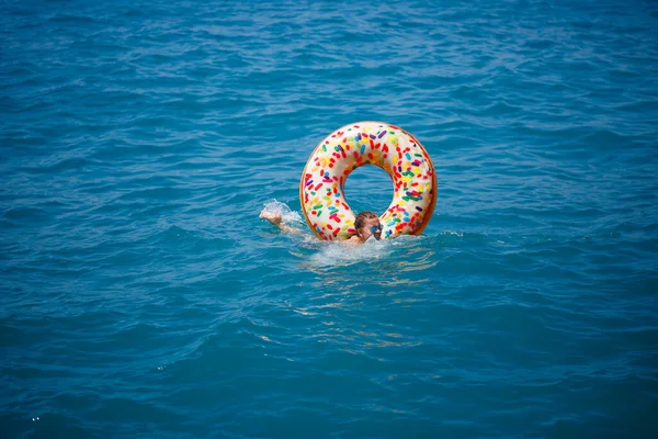 Young woman floating on an inflatable big donut in the transparent turquoise sea. View of a slender lady relaxing on vacation in Turkey, Egypt, Mediterranean Sea.