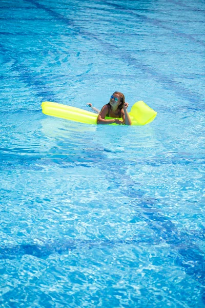 Junge sexy Mann im Badeanzug schwimmt im Pool auf einer aufblasbaren Matratze. Mädchen mit Sonnenbrille im blauen Pool im Urlaub — Stockfoto